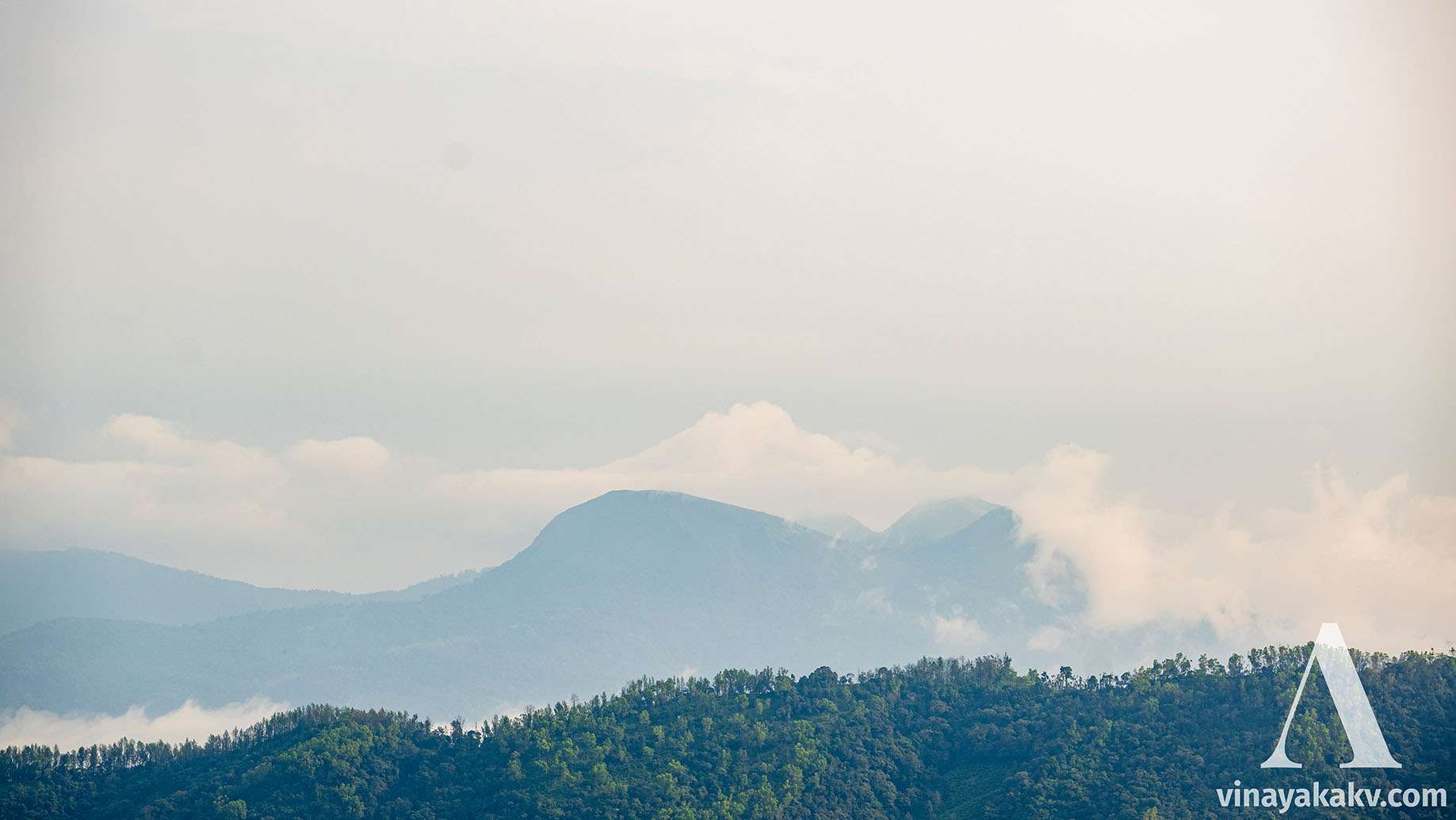 At the front, 2 peaks of _Mertiparvata_. The third peak is occuluded, the 4th one is visible with its head covered in the mist. The 5th and the tallest is completly covered with mist, although the cloud is in the same shape of the conical peak.